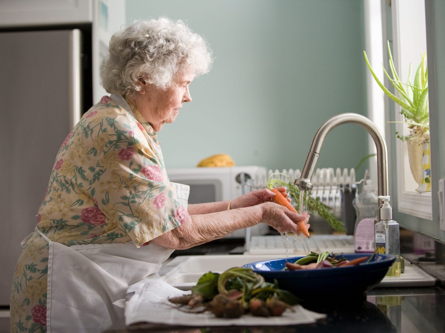 woman wearing yellow and pink floral dress wahing carrots