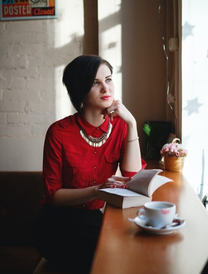 woman leaning on brown wooden table while holding book