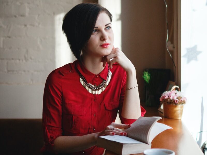 woman leaning on brown wooden table while holding book