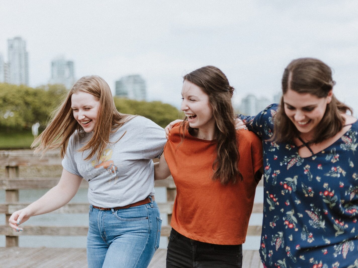 three women walking on brown wooden dock near high rise building during daytime