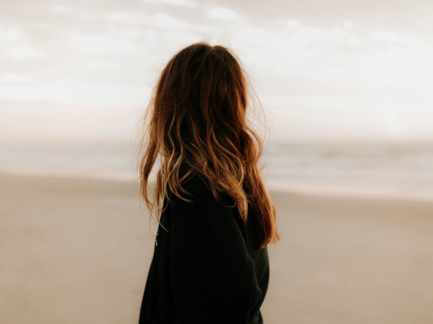 woman in black jacket standing on beach during daytime