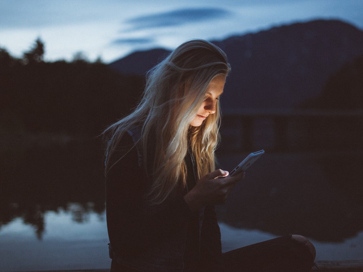 woman looking at phone beside body of water