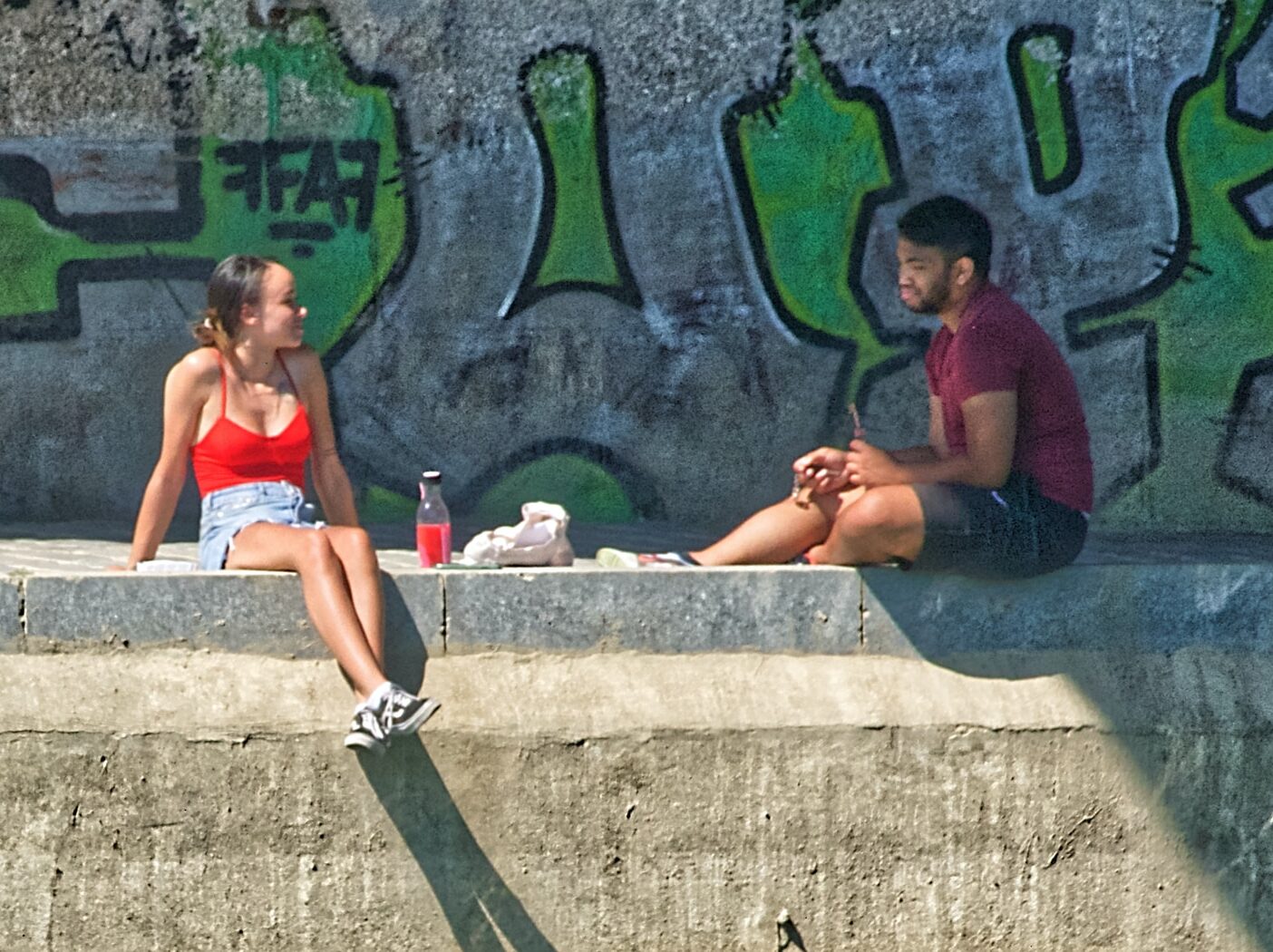 woman in red bikini sitting on concrete bench beside pool during daytime