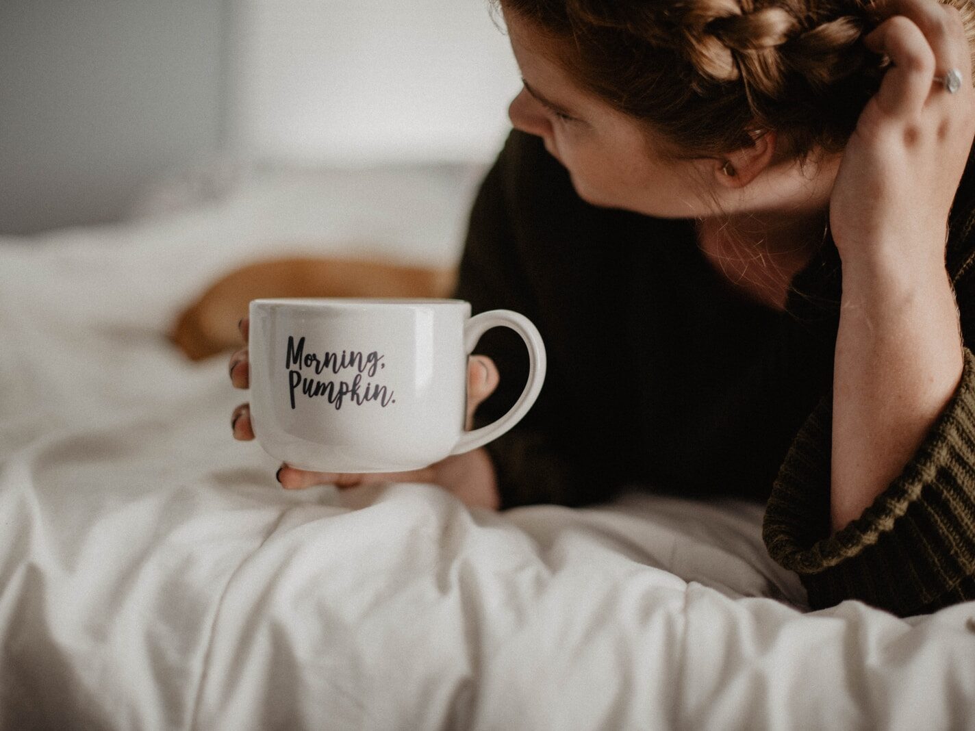 woman holding white mug while lying on bed
