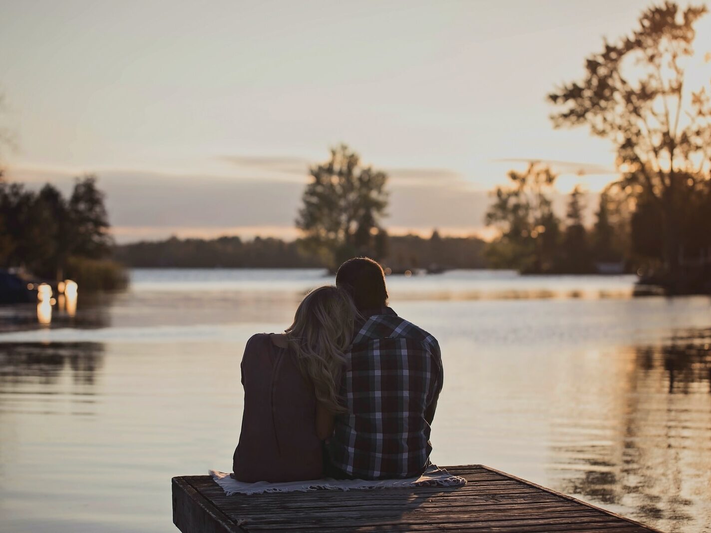 man and woman sitting on dock during golden hour