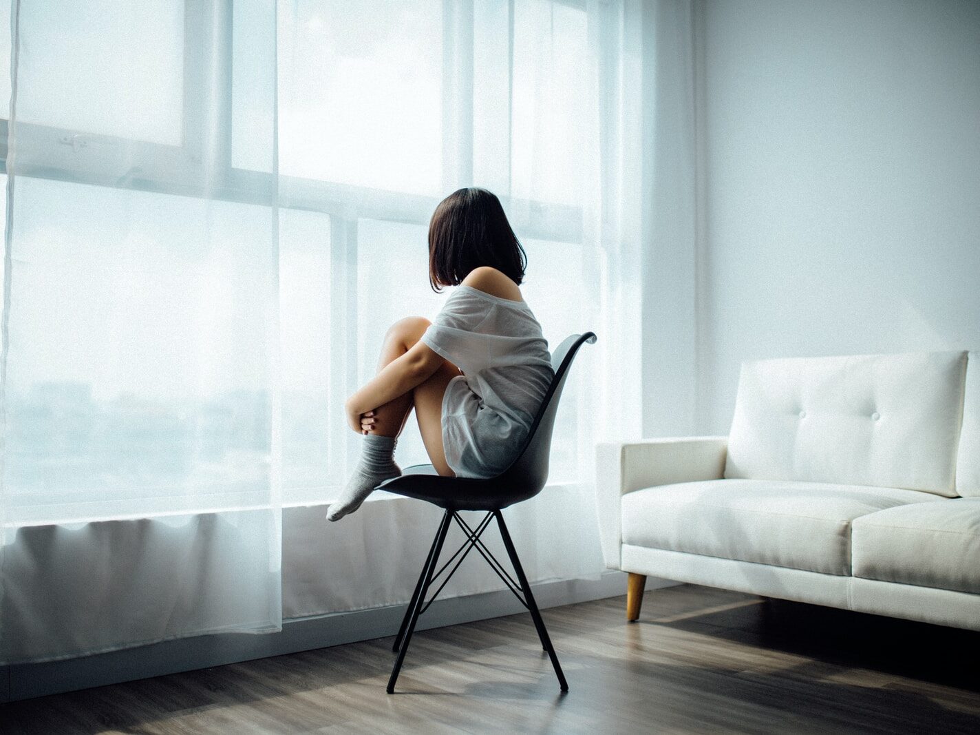 woman sitting on black chair in front of glass-panel window with white curtains