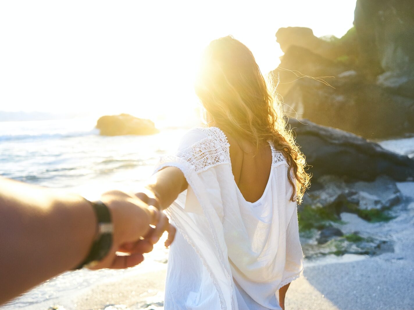 person holding woman's hand beside sea while facing sunlight