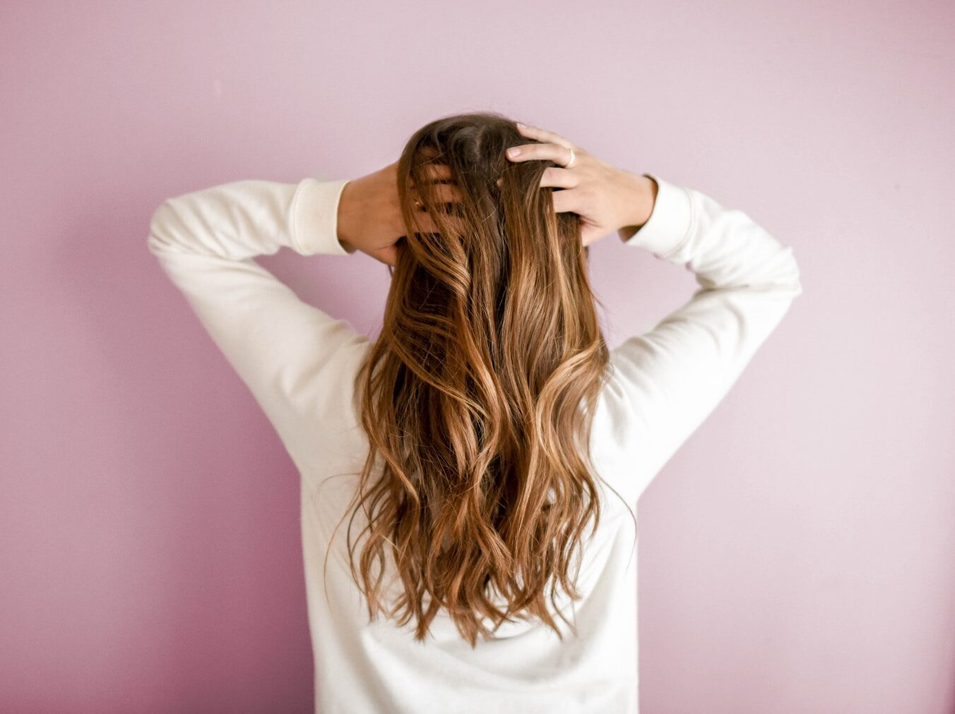 woman in white long-sleeved shirt standing in front of pink wall