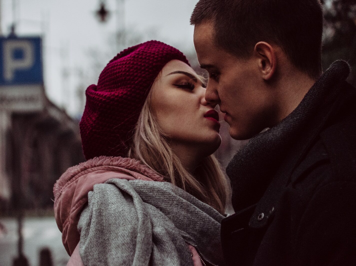 man and woman standing while kissing beside street signage