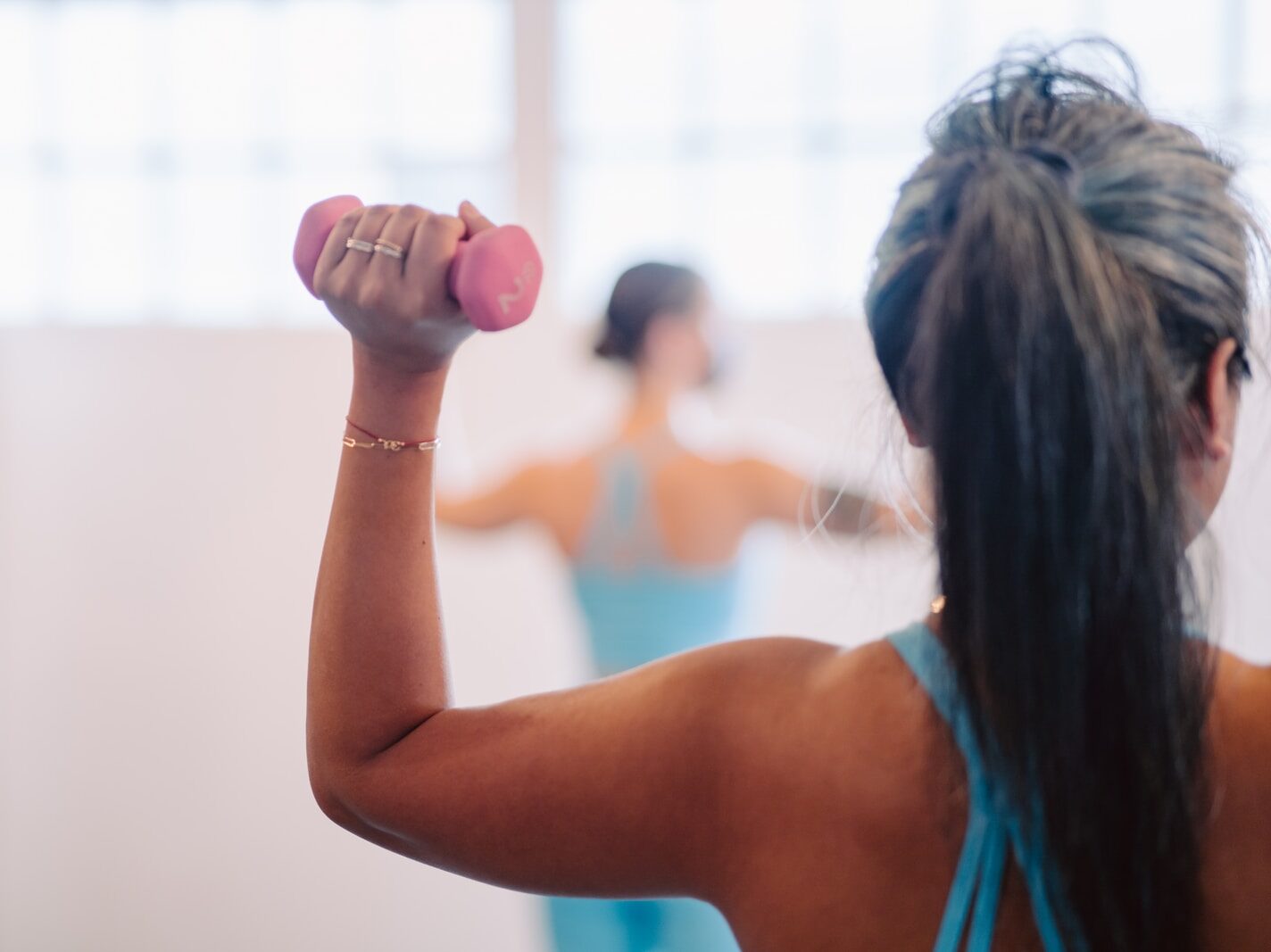 woman in blue tank top holding pink dumbbell