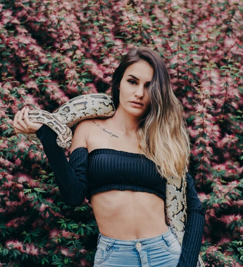 woman holding python snake near pink petaled flowers