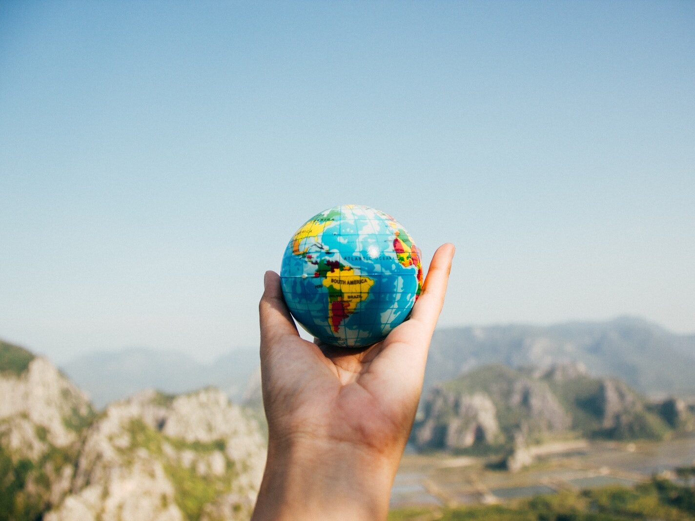 Person Holding World Globe Facing Mountain