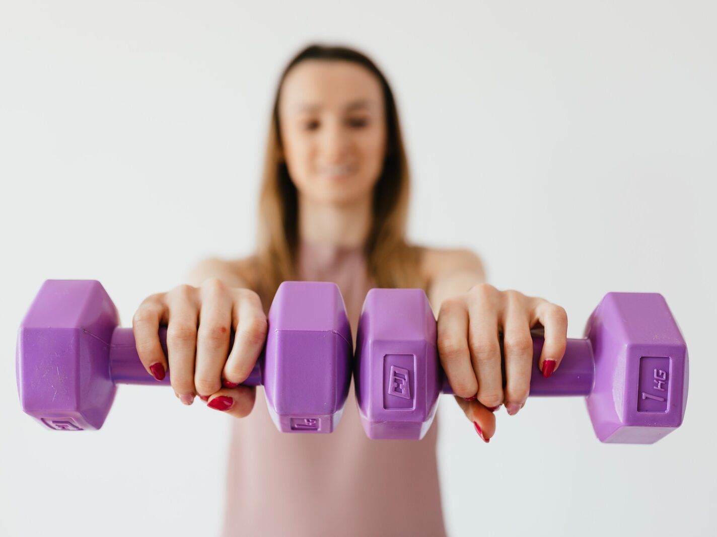 Defocused content young female doing bicep exercise with dumbbells during functional training in light studio