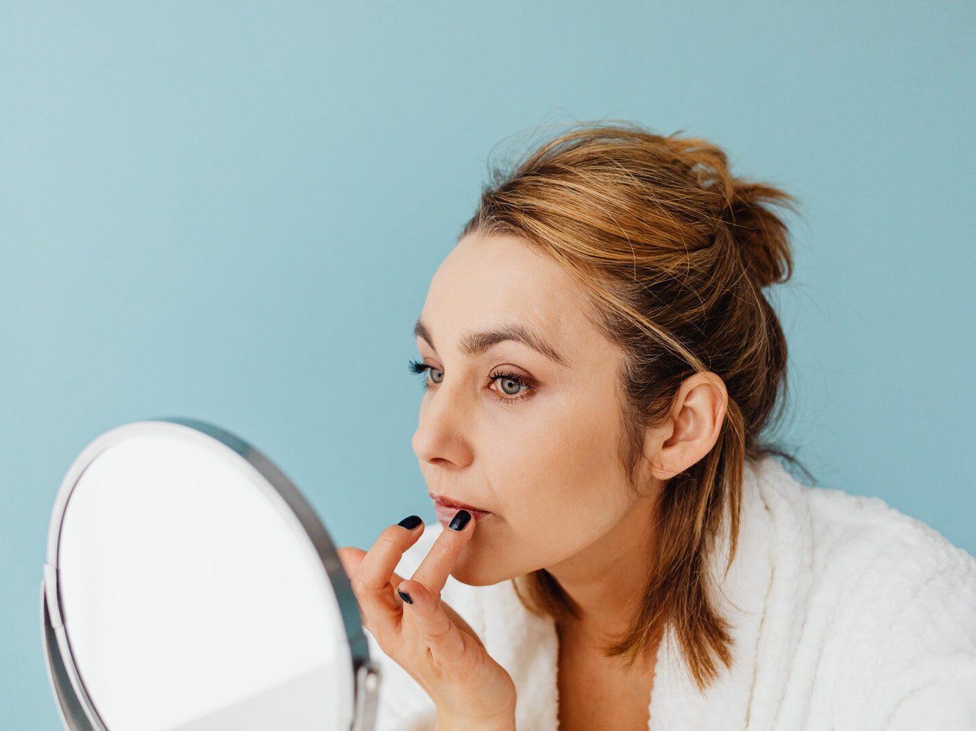 A Woman Applying a Cream on Her Lips while Looking at the Mirror