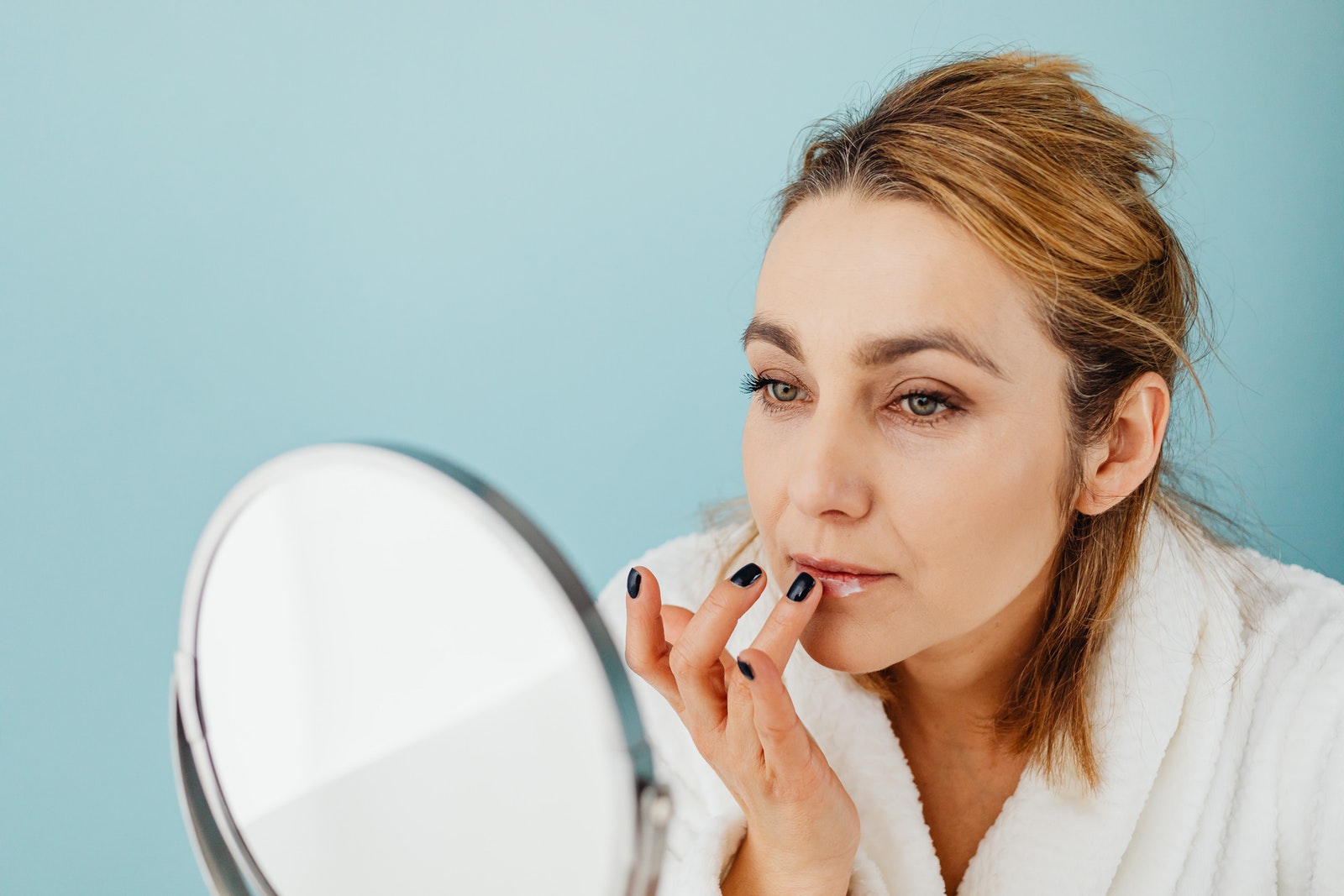 A Woman Applying a Cream on Her Lips while Looking at the Mirror