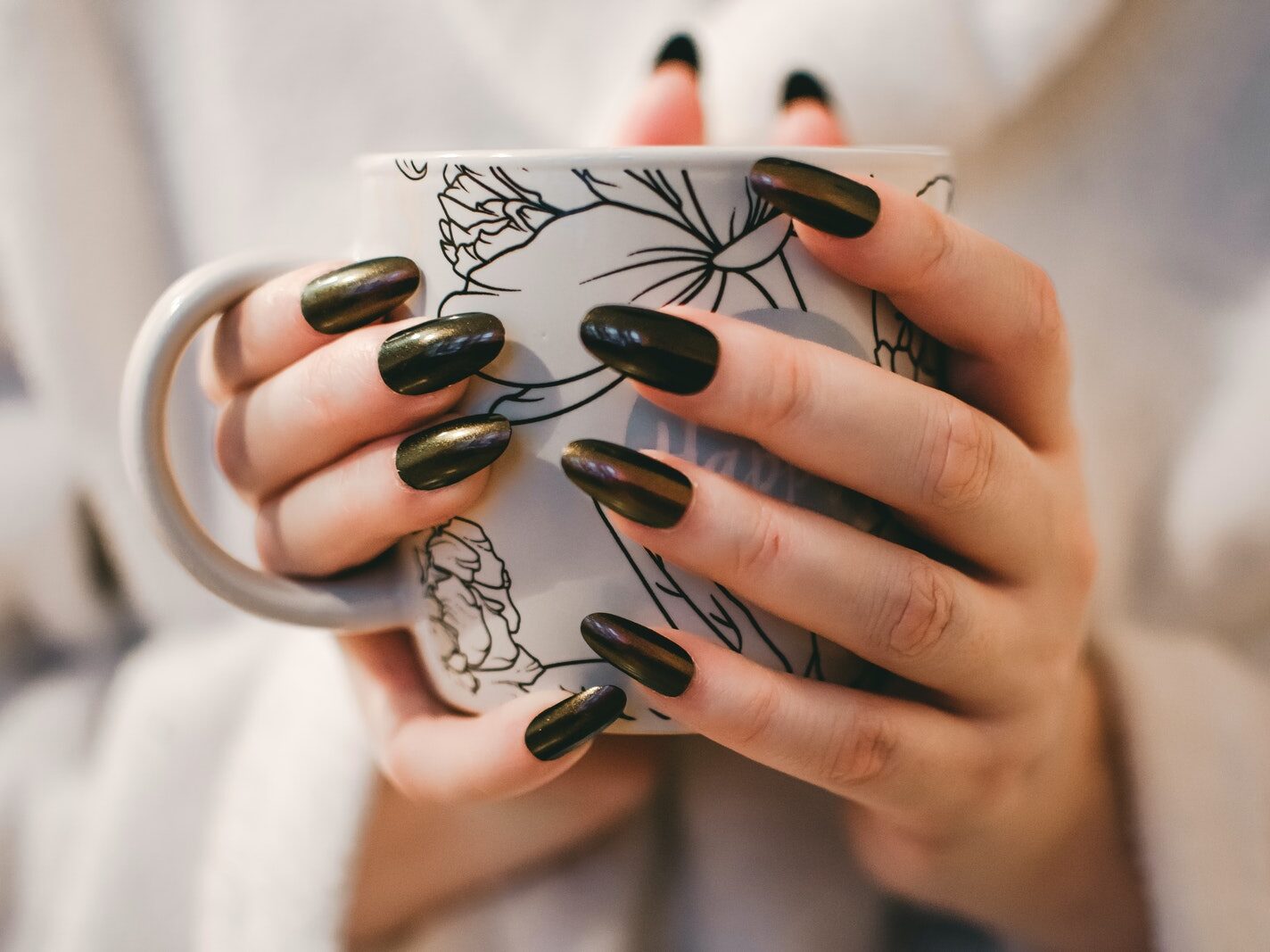 Woman With Black Manicure Holding White and Grey Floral Ceramic Cup