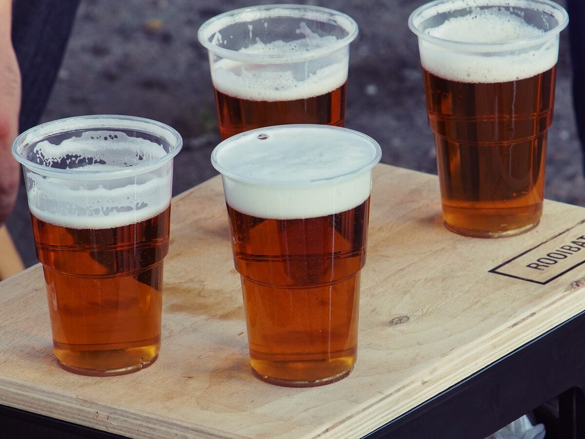four clear plastic disposable cups with beer on the top of the board