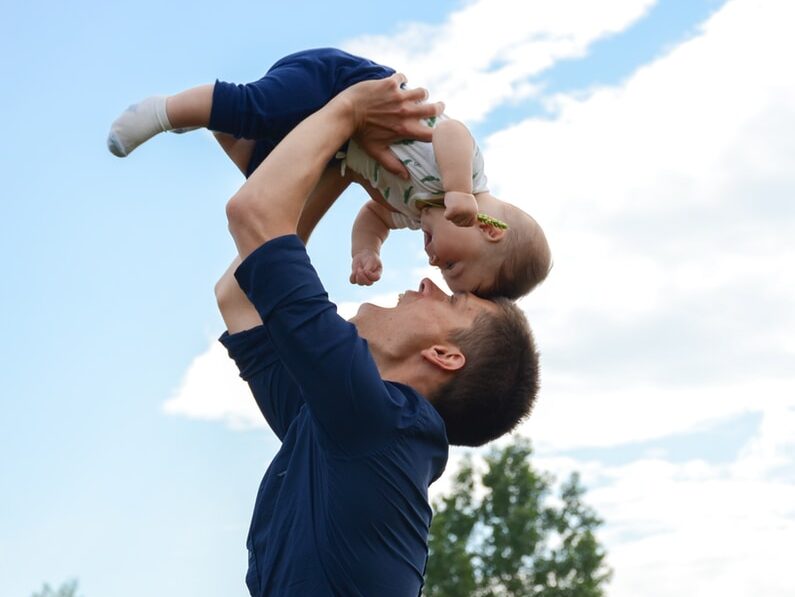 man in blue long sleeve shirt carrying baby in white onesie