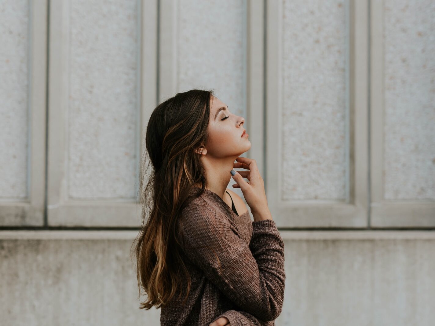woman in brown long-sleeved top standing beside wall