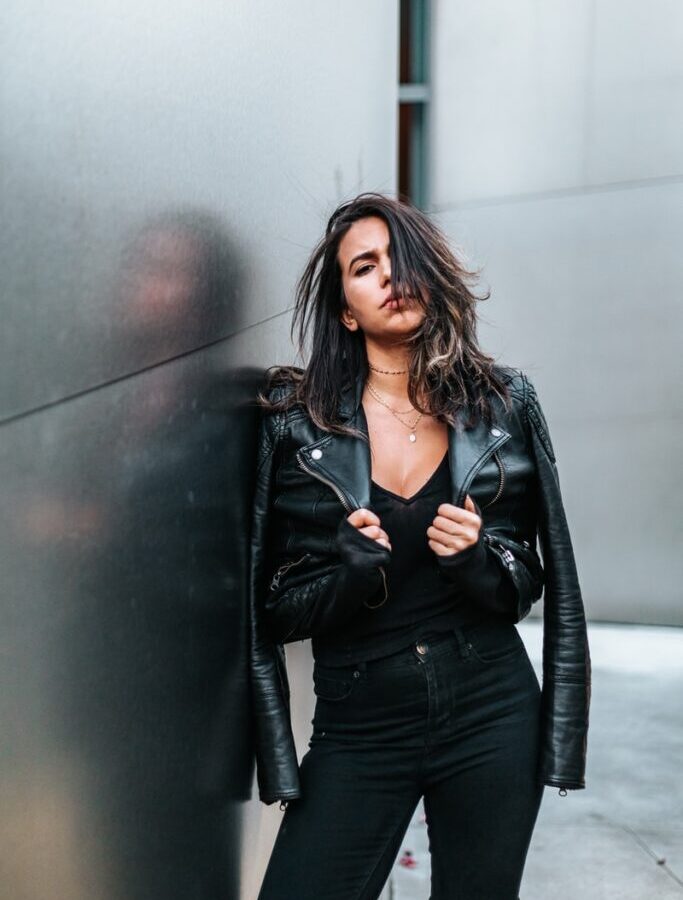 woman touching her black leather jacket while standing near silver wall