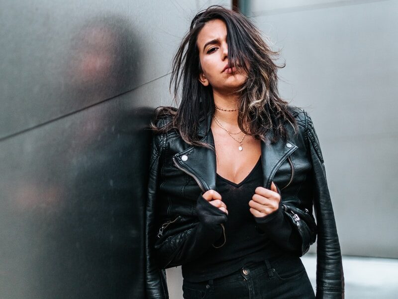 woman touching her black leather jacket while standing near silver wall