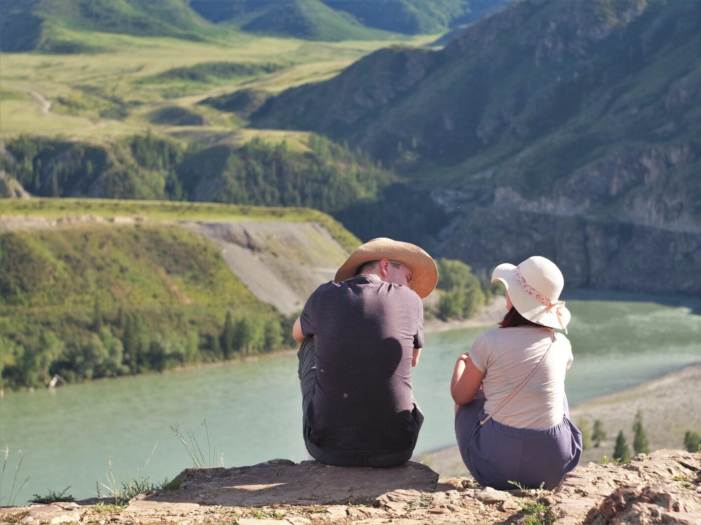 woman in black tank top and white pants sitting on brown rock near lake during daytime