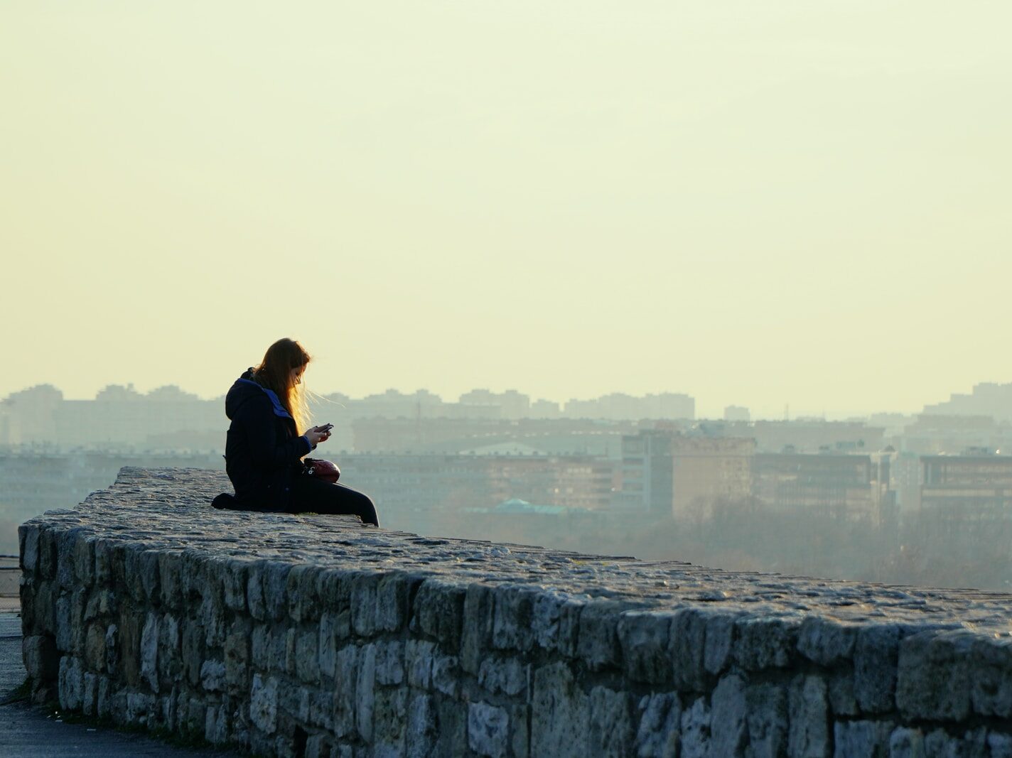 woman in black jacket sitting on gray concrete wall during daytime