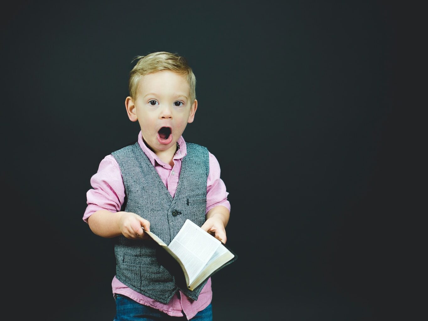 boy wearing gray vest and pink dress shirt holding book