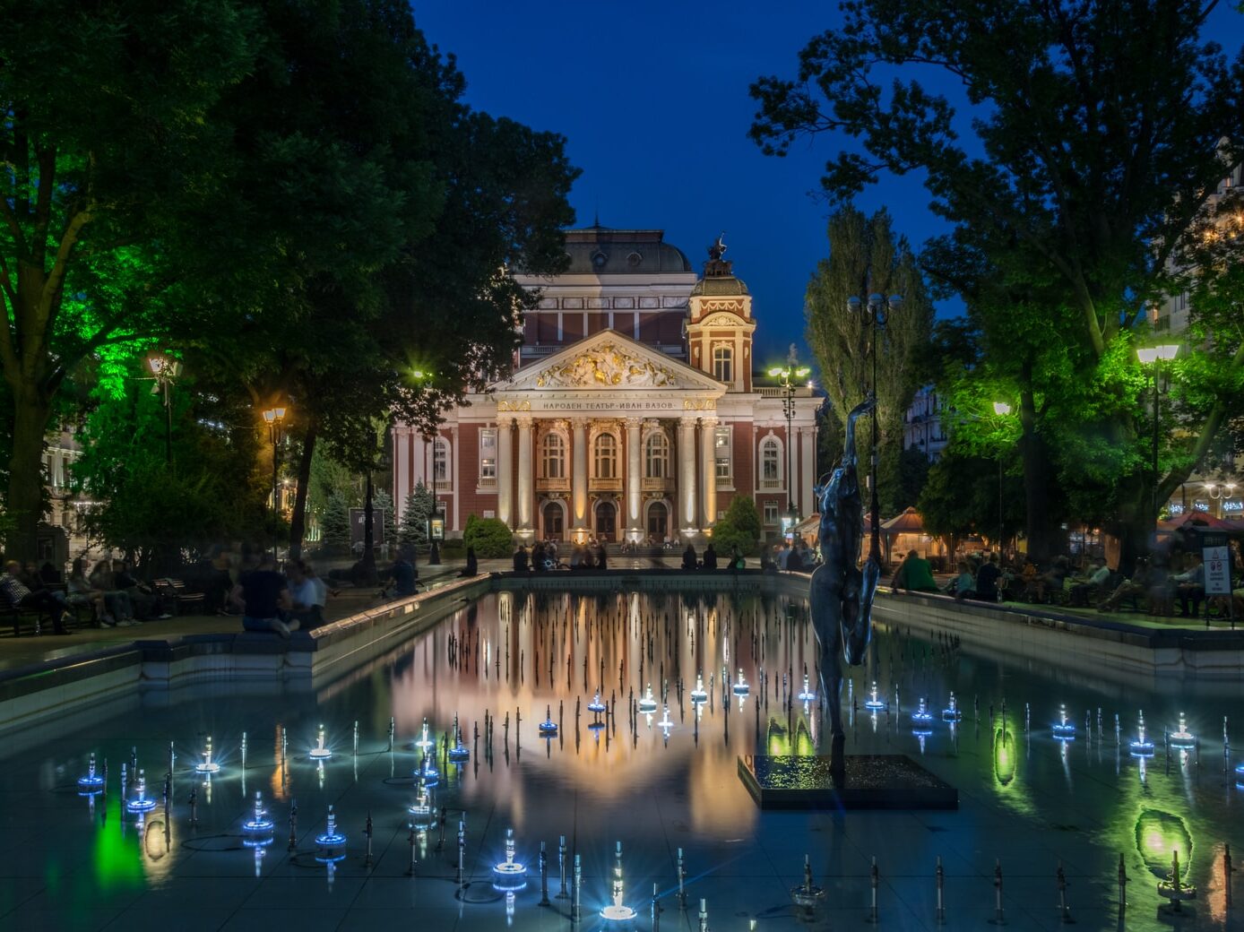 brown mansion house near rectangular swimming pool surrounded with tall and green trees during night time