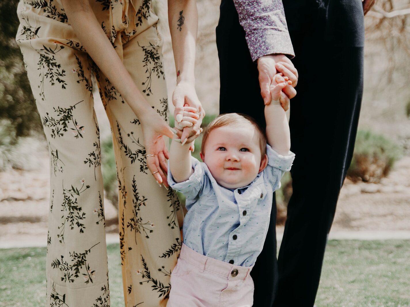 man and woman holding hand of toddler walking on grass field