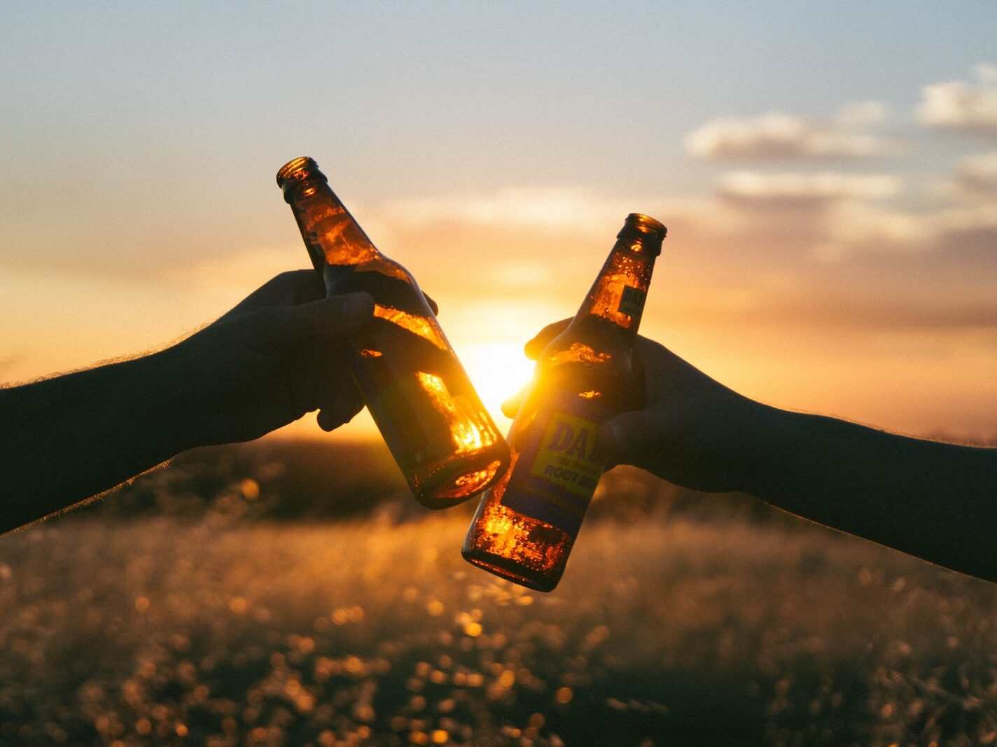 photography of person holding glass bottles during sunset
