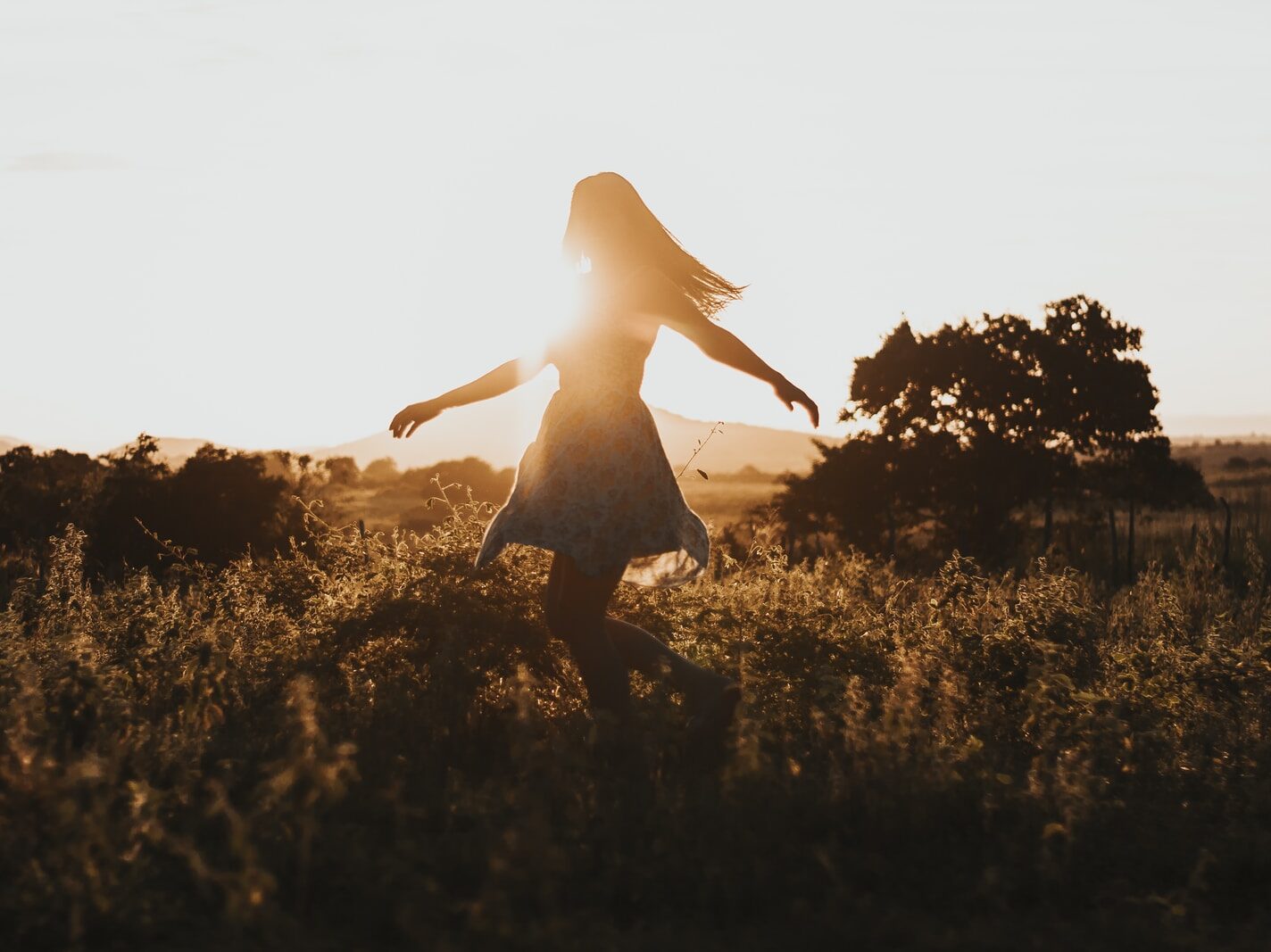 silhouette of woman dancing in the middle of grass field