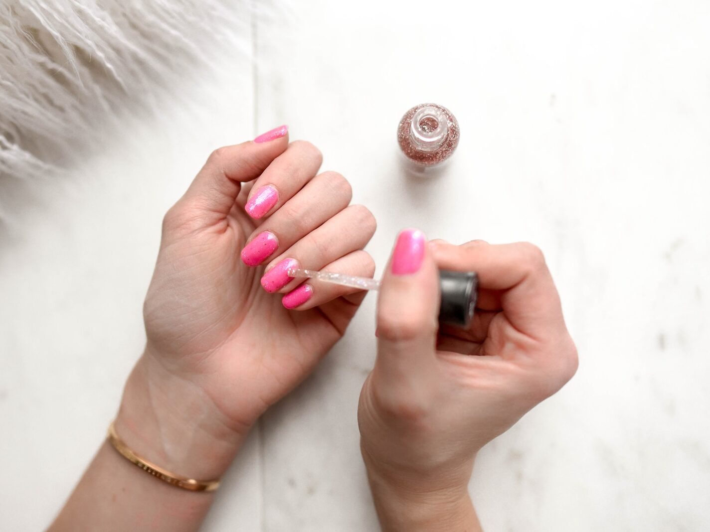 person spreading glittered nail polish on pink nails