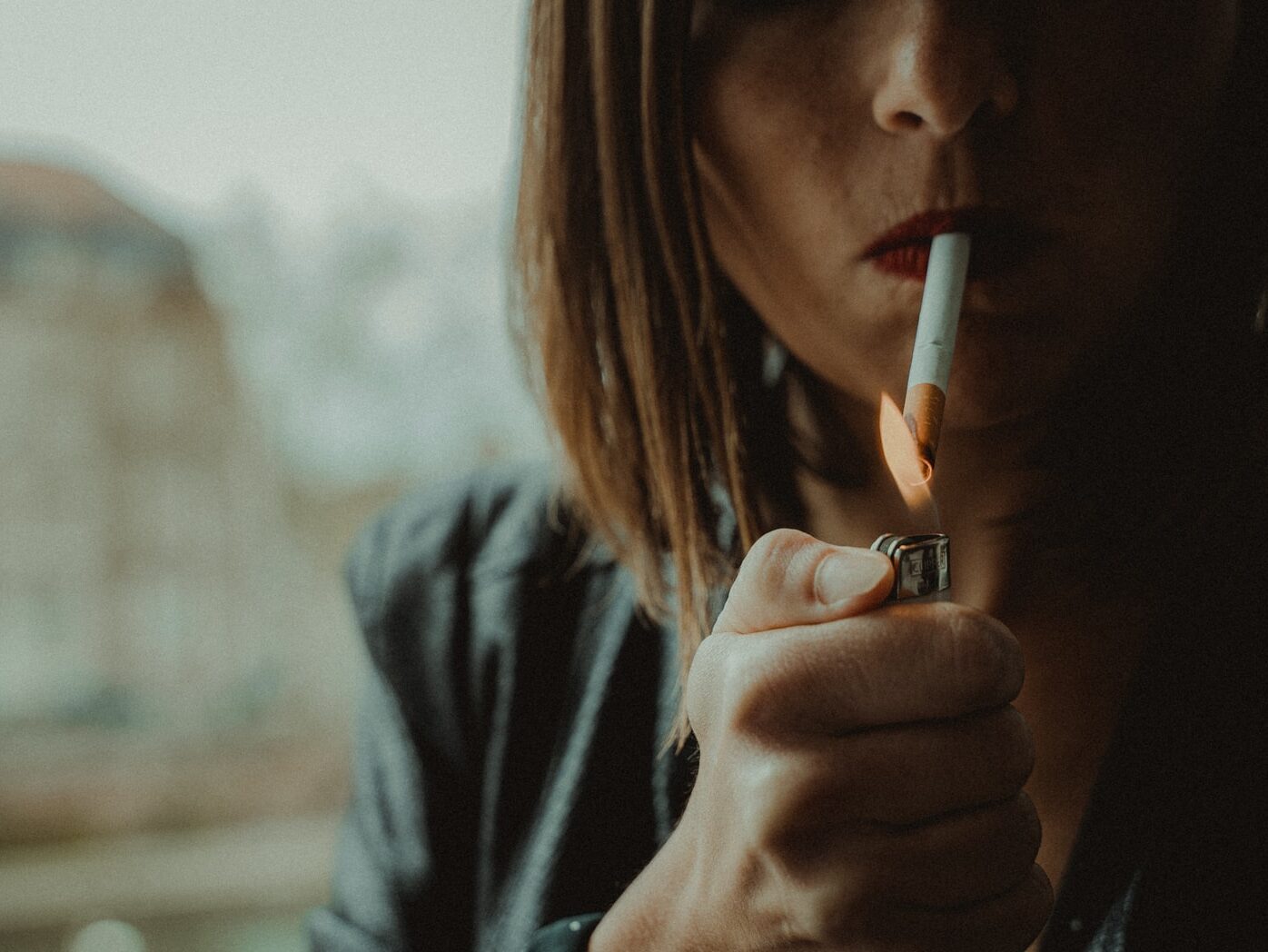 woman in black jacket holding orange disposable lighter
