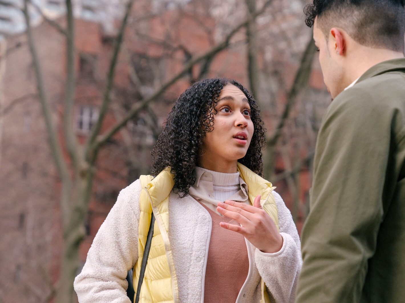From below of ethnic female with short curly hair standing and arguing with boyfriend on street in daylight