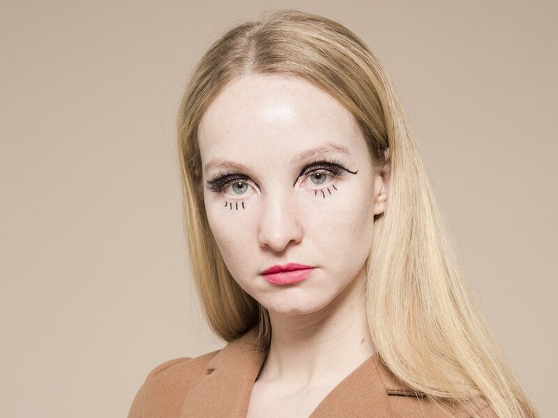 Emotionless female with extraordinary makeup on face looking at camera on beige background of studio