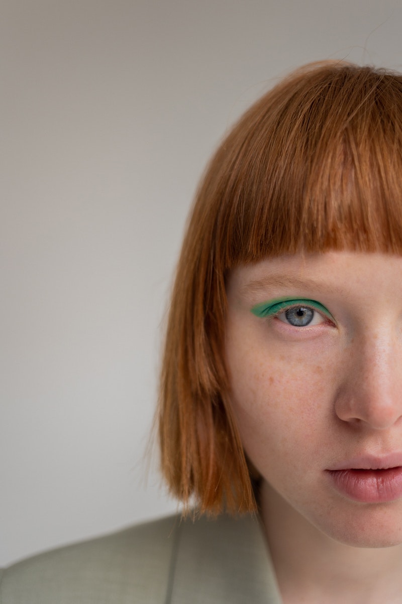 Crop young female with ginger hair and blue eyes looking at camera against gray background