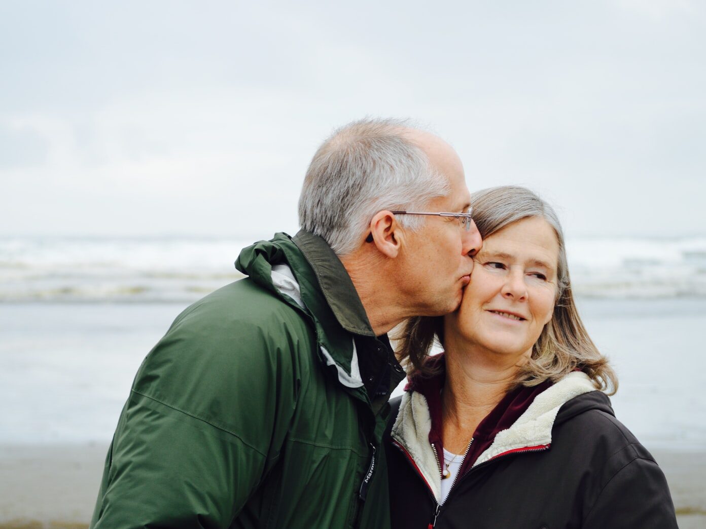 man kissing woman on check beside body of water
