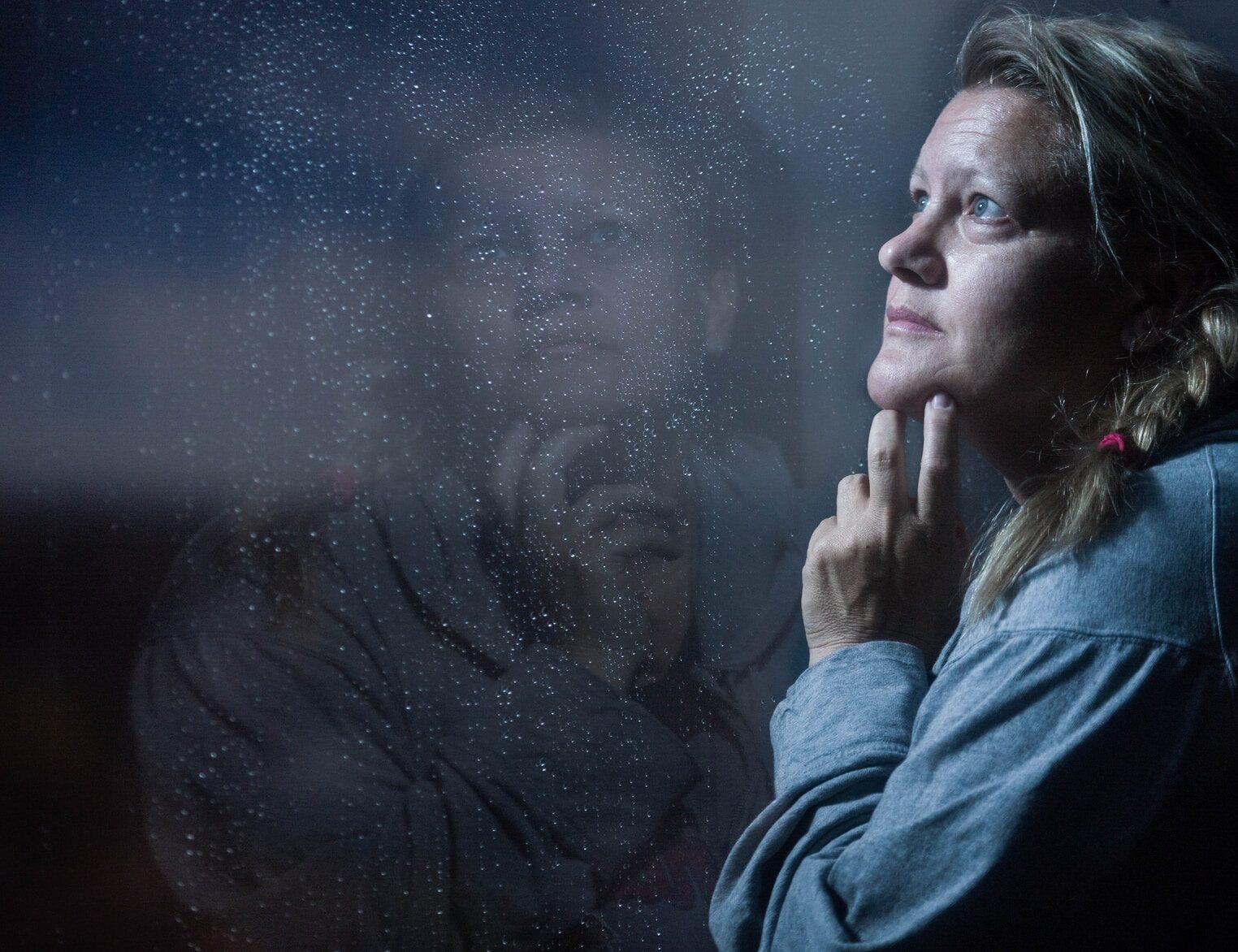 clear glass window panel casting reflection of woman touching her jaw