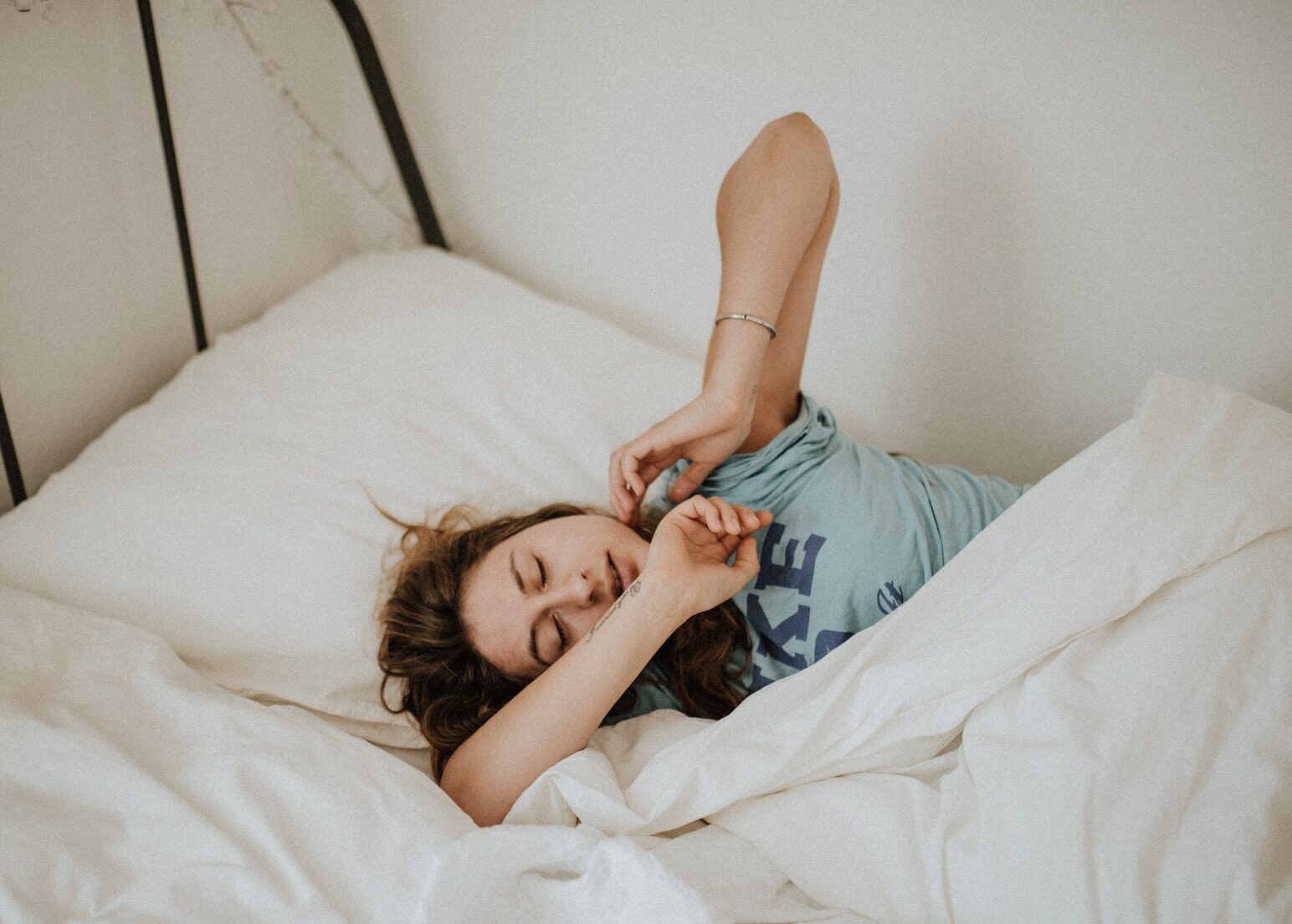 woman covered in white blanket sleeping on white bed comforter