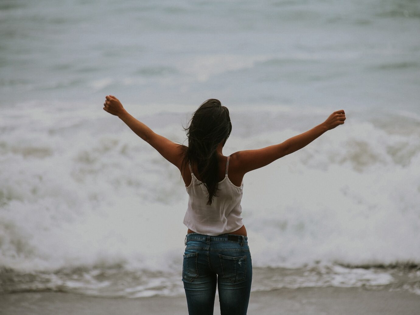woman in white spaghetti strap top standing on the seashore