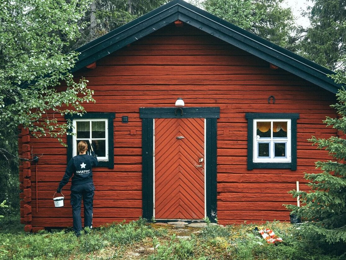 man in black jacket standing beside brown wooden house during daytime