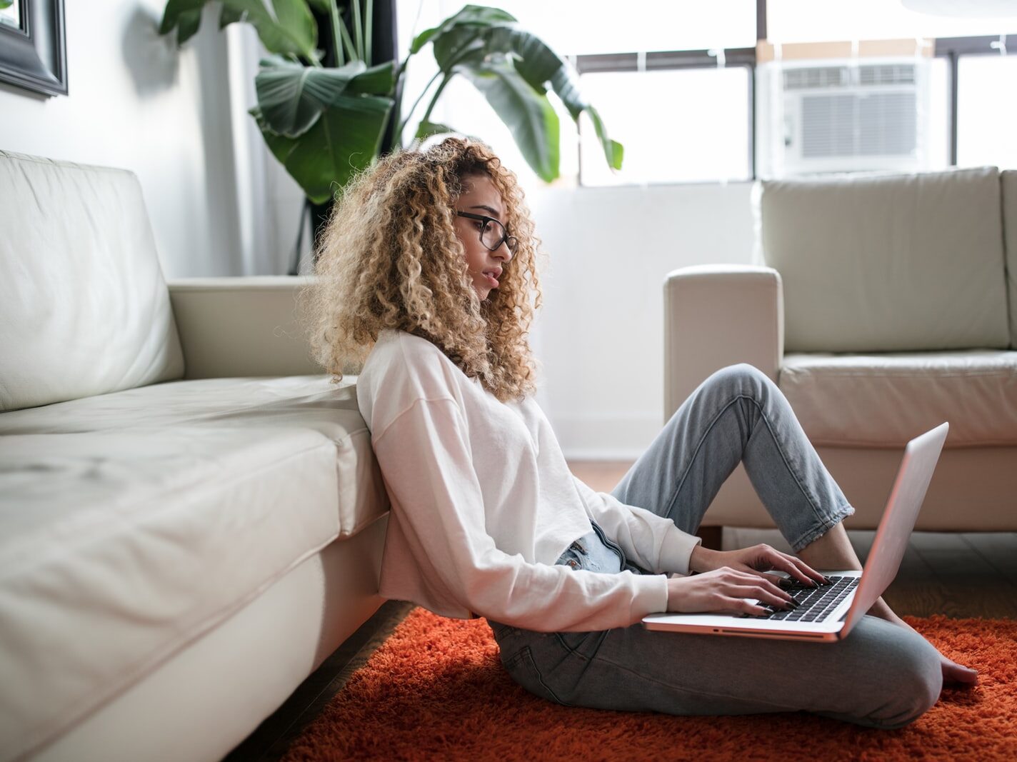 woman sitting on floor and leaning on couch using laptop