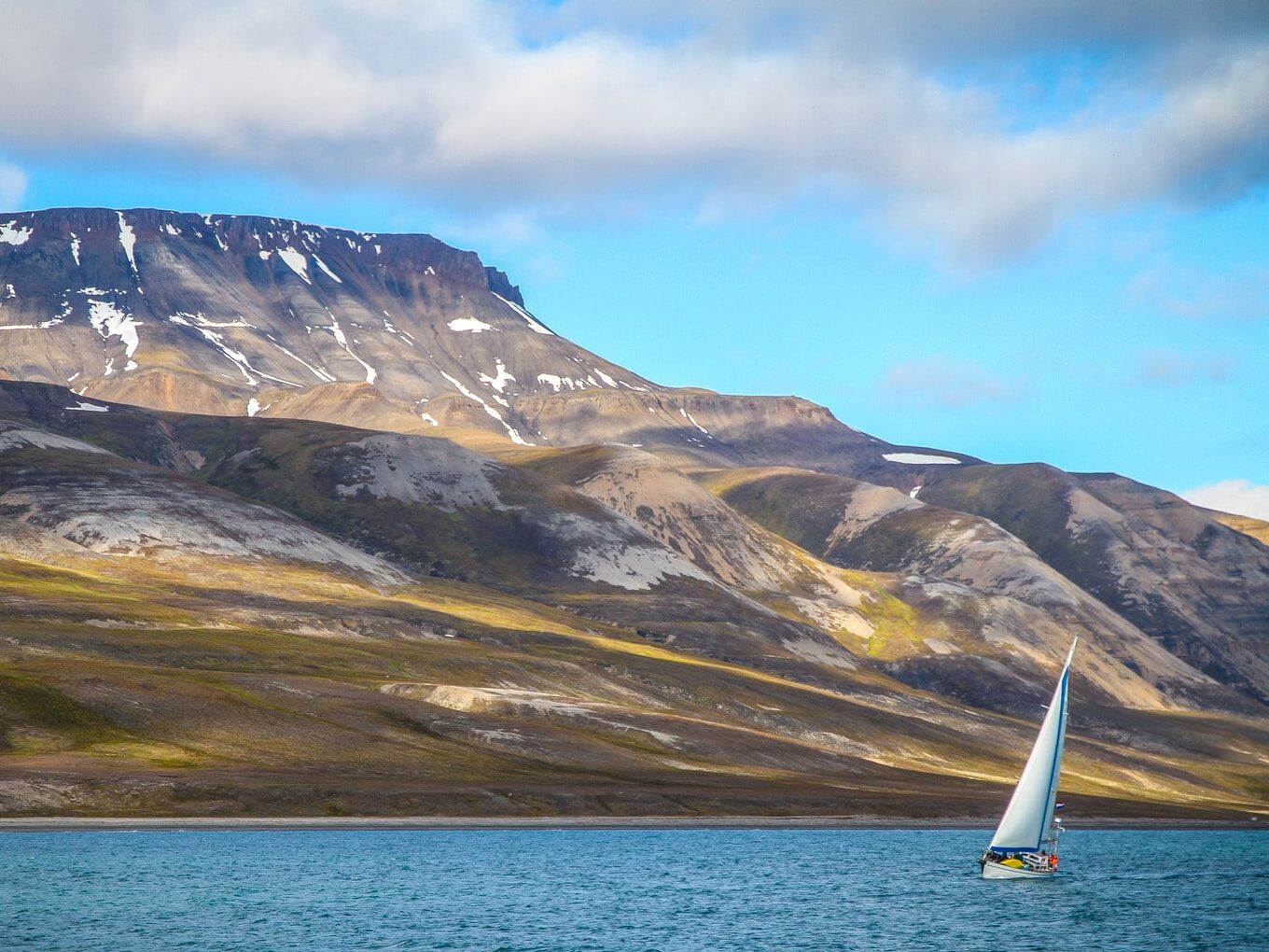 sailing boat on ocean with snow-capped mountain at distance