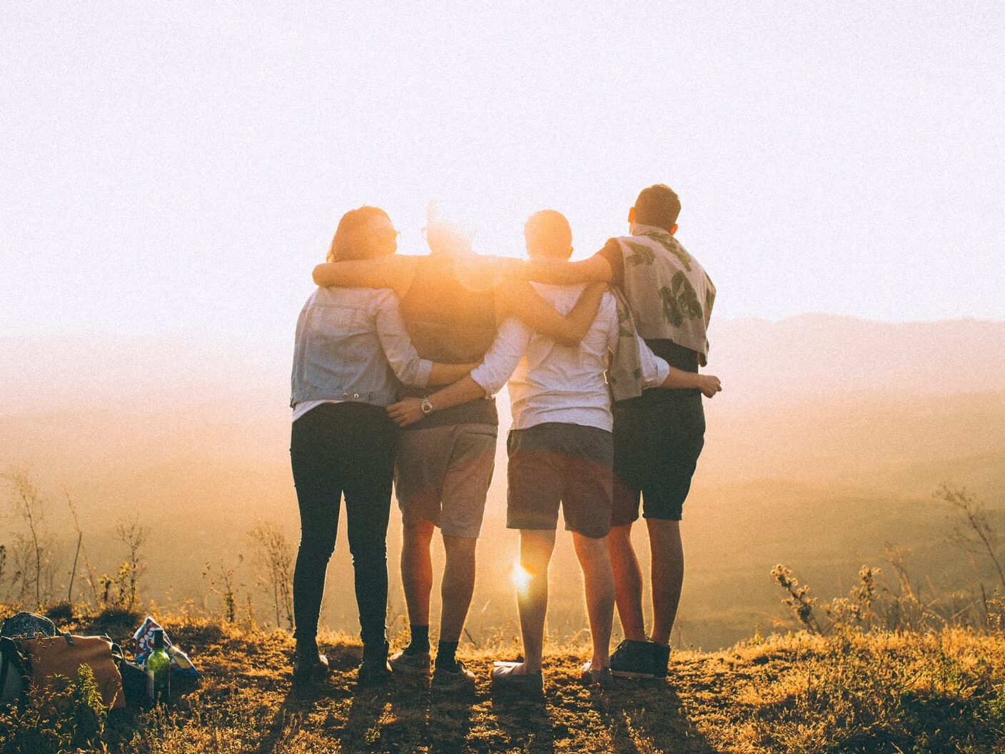 four person hands wrap around shoulders while looking at sunset