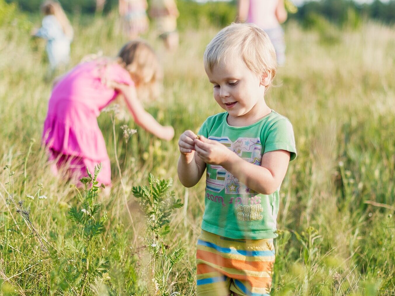girl in pink t-shirt standing on green grass field during daytime