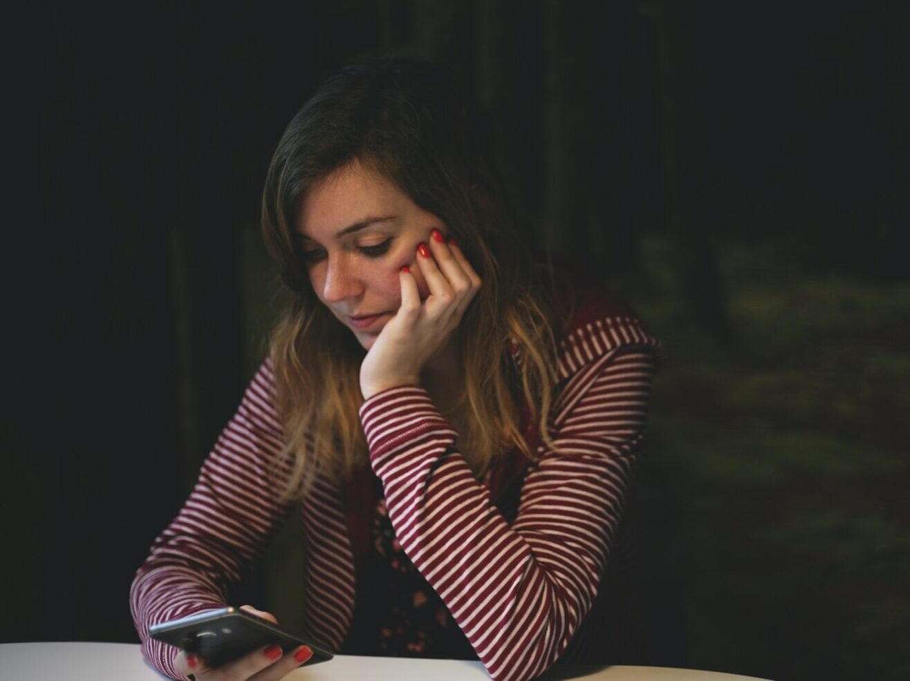 woman leaning on white wooden table while holding black Android smartphone