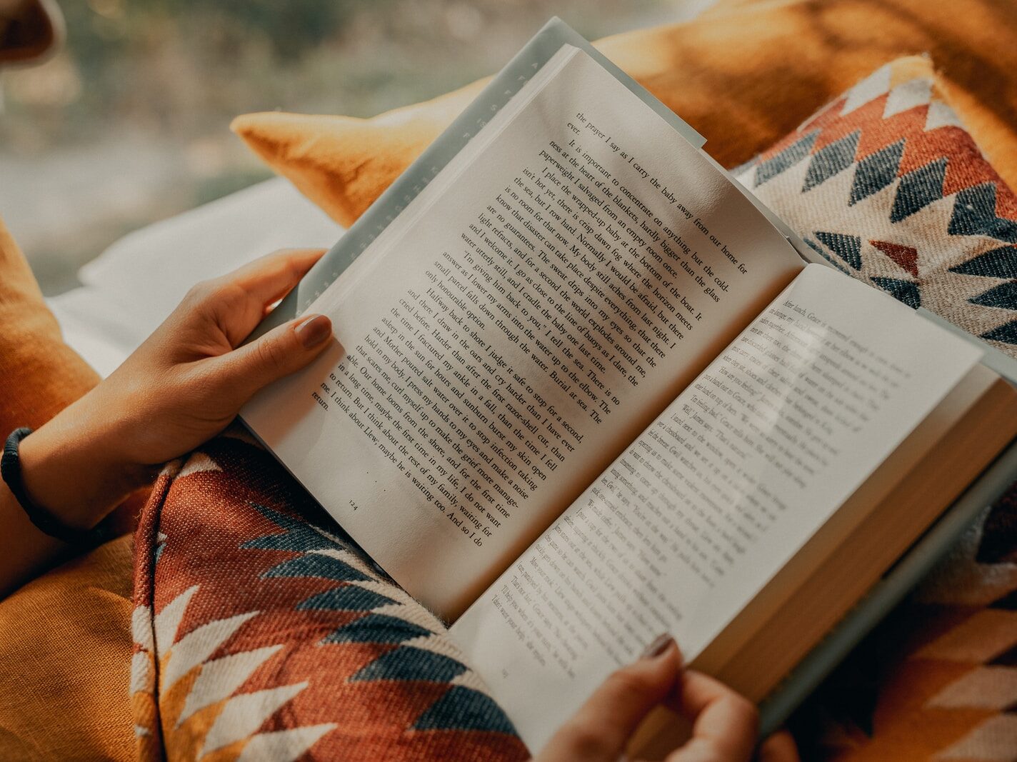 person reading book on brown and beige textile