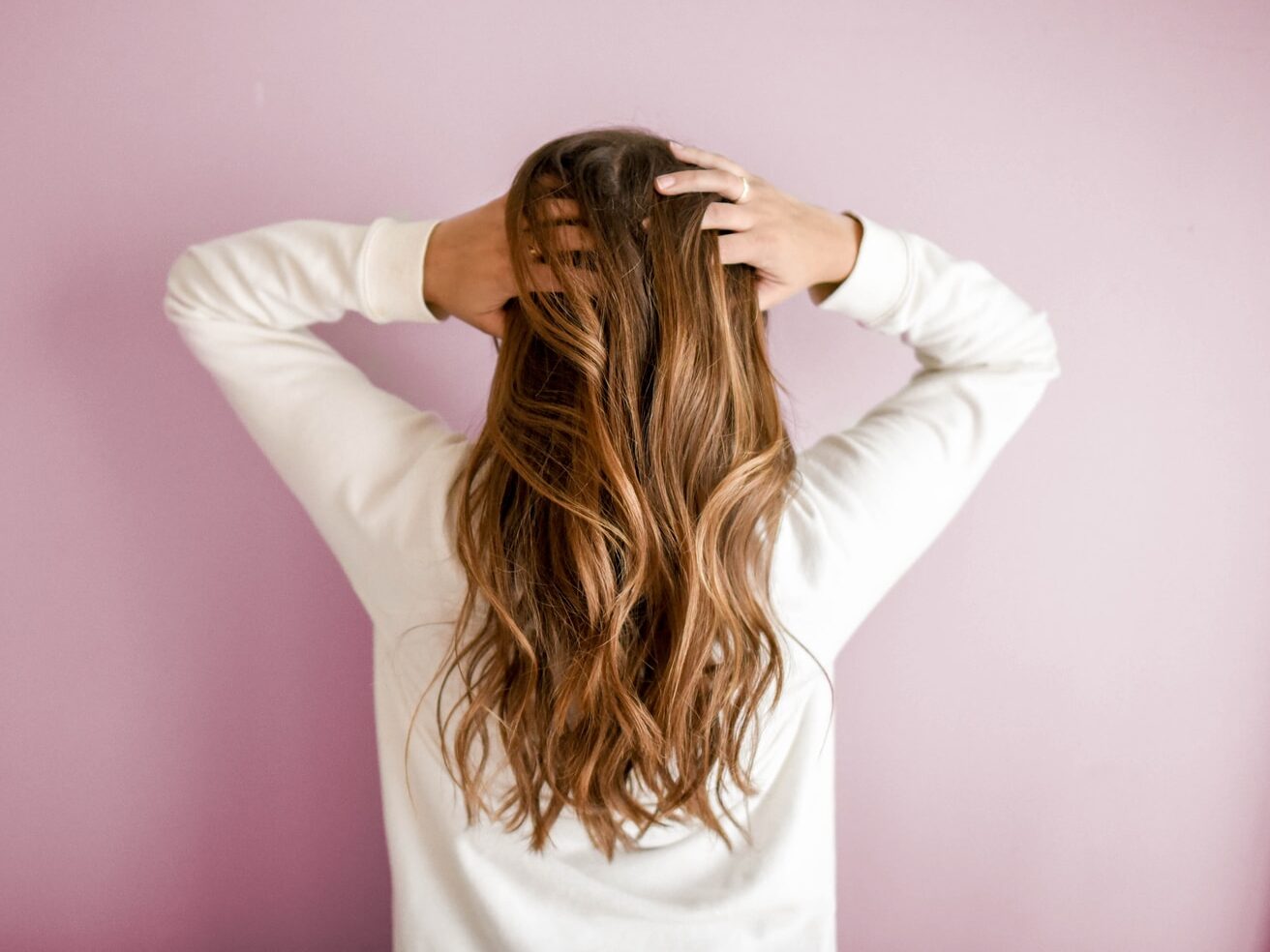 woman in white long-sleeved shirt standing in front of pink wall