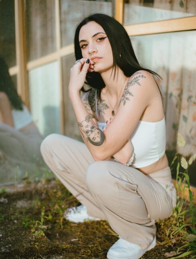 Woman in White Tank Top and White Pants Sitting on Green Grass